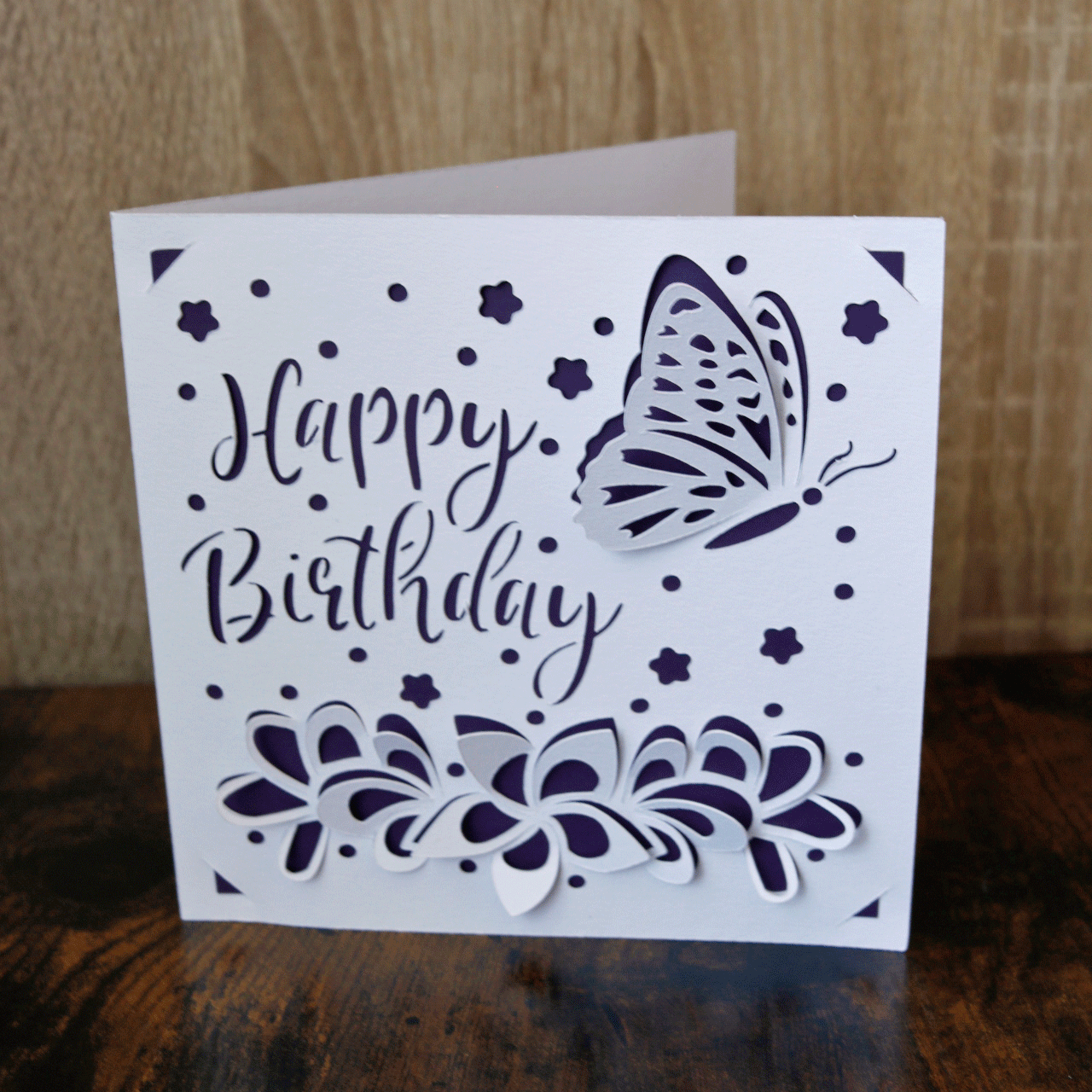 Geburtstagskarte "Schmetterling im Blumenfeld" dunkel violett-weiß, mit dem Schriftzug Happy Birthday sowie Blumen und einem Schmetterling in 3D-Optik.