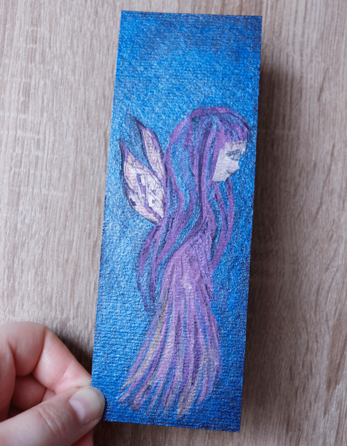 Ein blau schimmerndes Lesezeichen mit einer Lila Fee