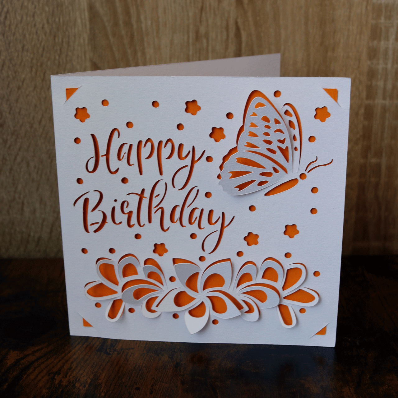 Geburtstagskarte "Schmetterling im Blumenfeld" orange-weiß, mit dem Schriftzug Happy Birthday sowie Blumen und einem Schmetterling in 3D-Optik. 