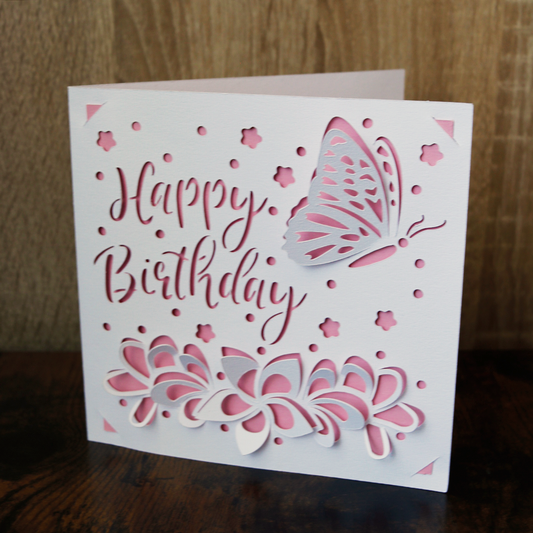 Geburtstagskarte "Schmetterling im Blumenfeld" rosa-weiß, mit dem Schriftzug Happy Birthday sowie Blumen und einem Schmetterling in 3D-Optik.